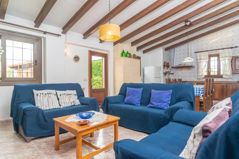 Una sala de estar con asientos azules, una mesa de centro de madera y una cocina abierta al fondo.