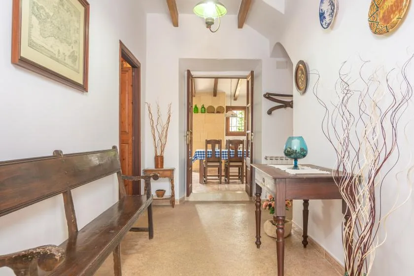 Un pasillo luminoso con bancos de madera y una mesa conduce a un comedor.