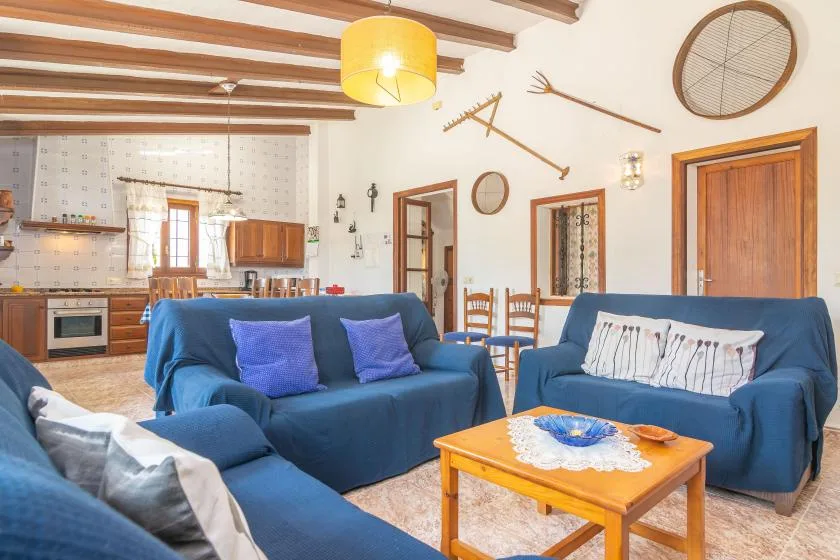 Una sala de estar con asientos azules, una mesa de centro de madera y una cocina al fondo.