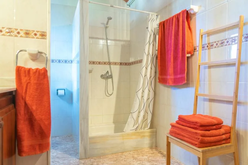 Un baño alicatado con ducha, cortina estampada y toallas naranjas.