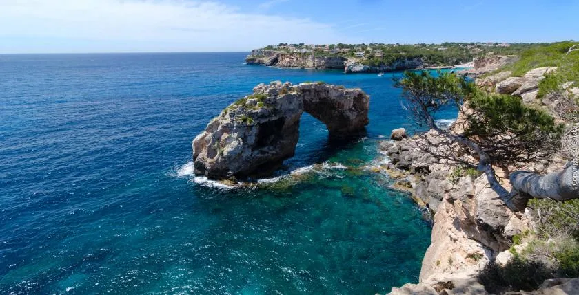 Una costa rocosa con un arco natural sobre aguas azules y transparentes.