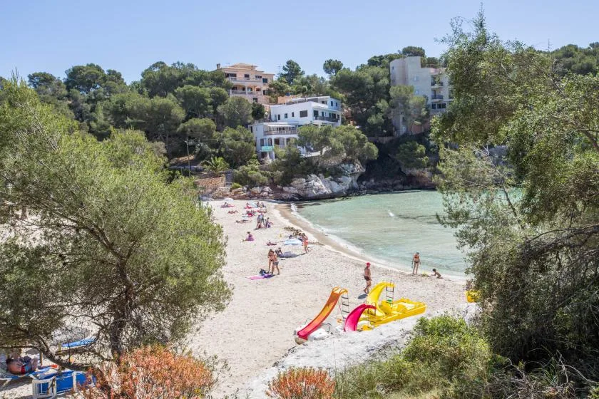 Una playa de arena bordea aguas claras, con hidropedales coloridos en la orilla.