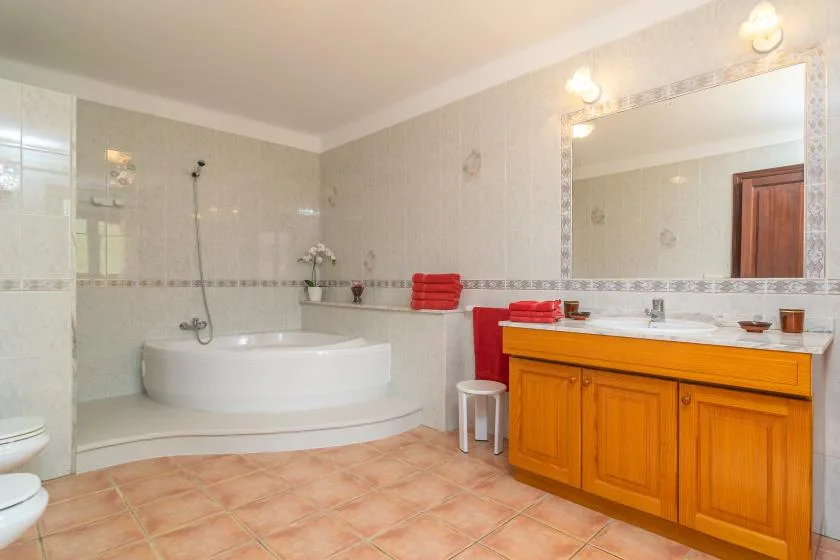 Un baño con azulejos, bañera y un mueble de madera bajo un espejo grande.