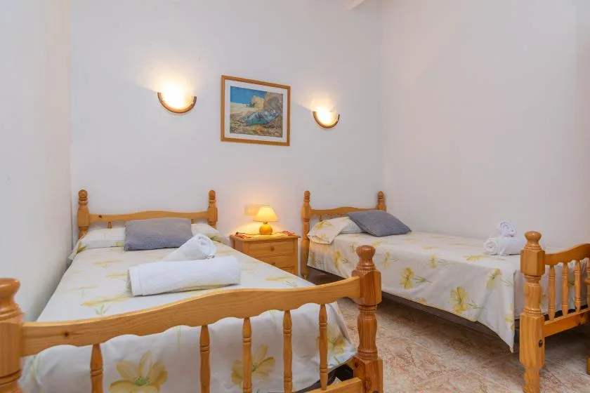 Un dormitorio con dos camas de madera, lámparas de mesilla y un cuadro enmarcado.