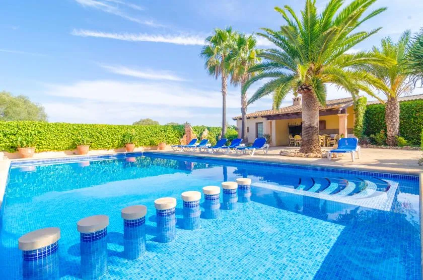 Una piscina exterior soleada con tumbonas azules y palmeras.