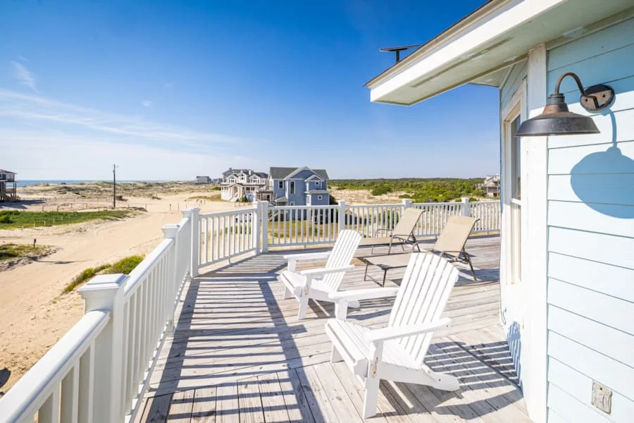 A sunlit deck with white seating overlooks a sandy coastal landscape.