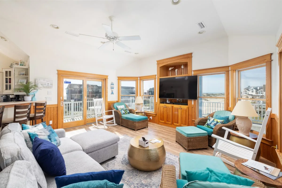 A bright living room with seating, a television, and large windows opening onto a balcony.