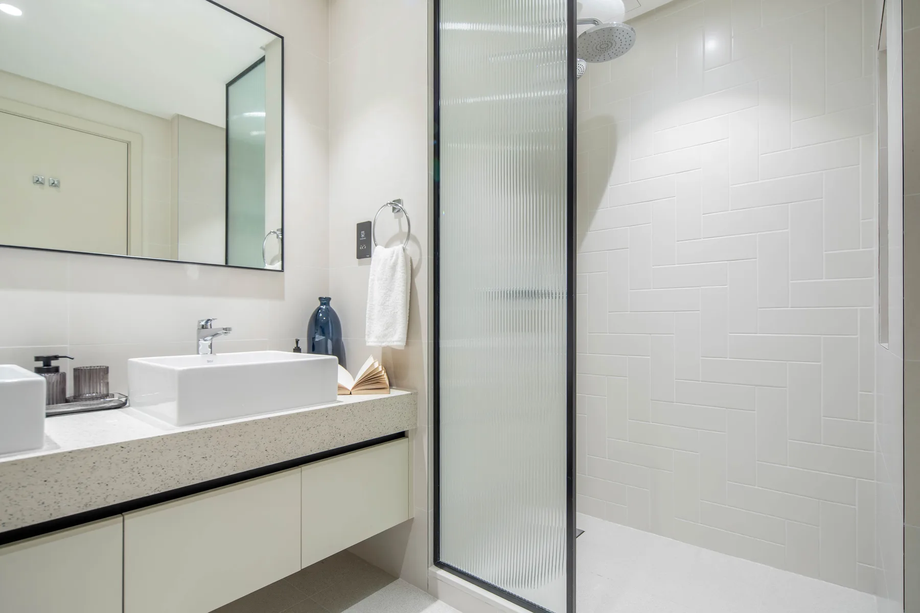Un baño luminoso con lavabo, espejo y zona de ducha con azulejos.