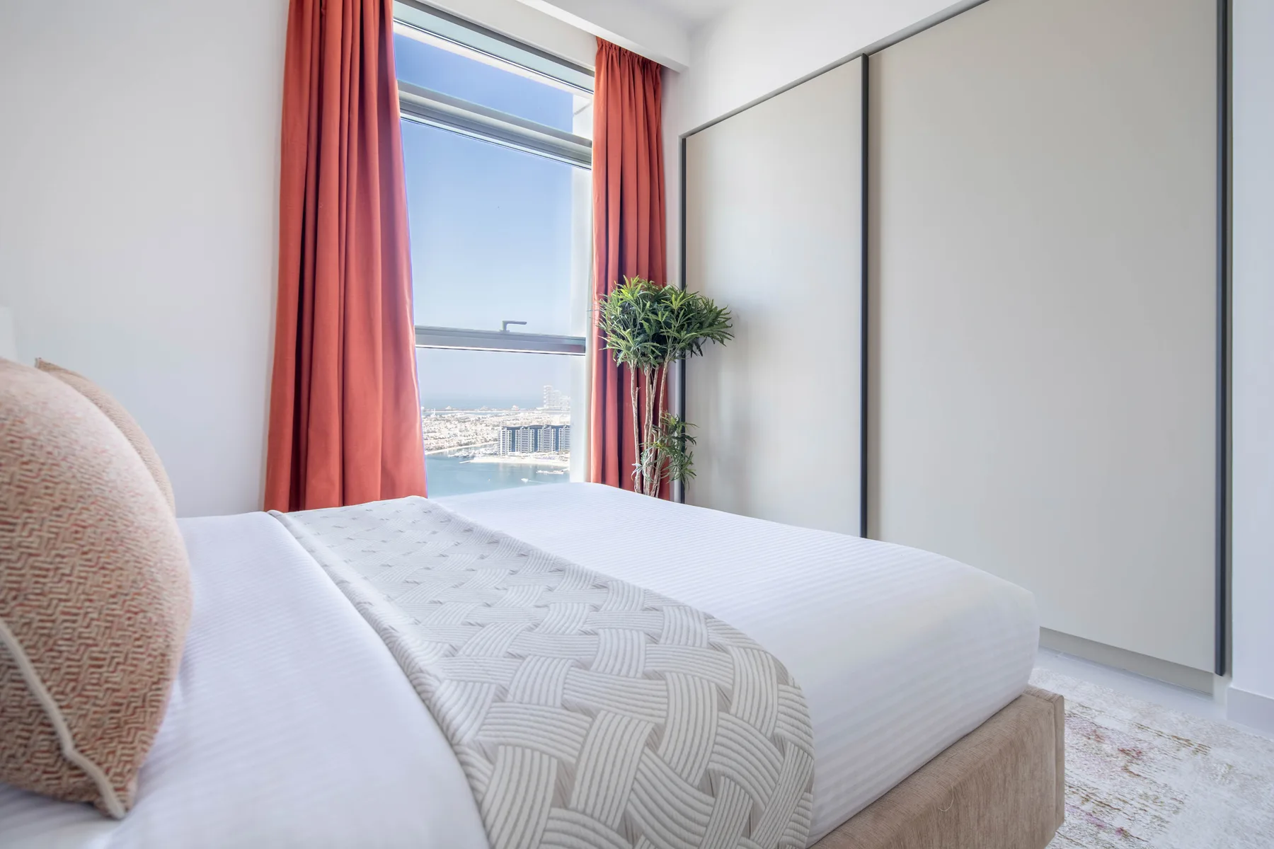 Un dormitorio con una cama tendida junto a una ventana grande con cortinas rojas.