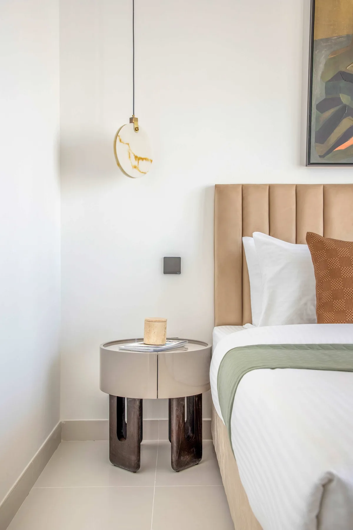Un dormitorio con una cama, un cabecero tapizado y una mesita redonda.