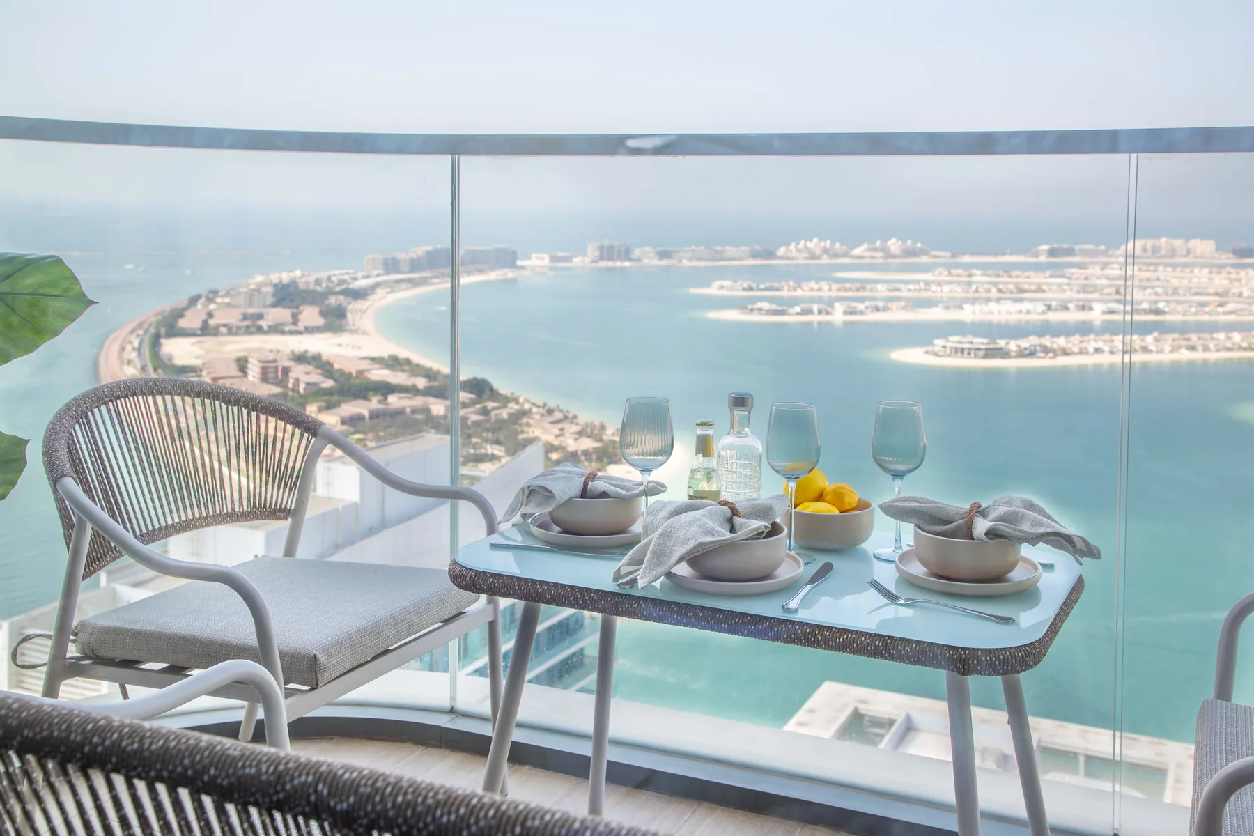 Una mesa de comedor y asientos en un balcón dan al mar y a edificios costeros.
