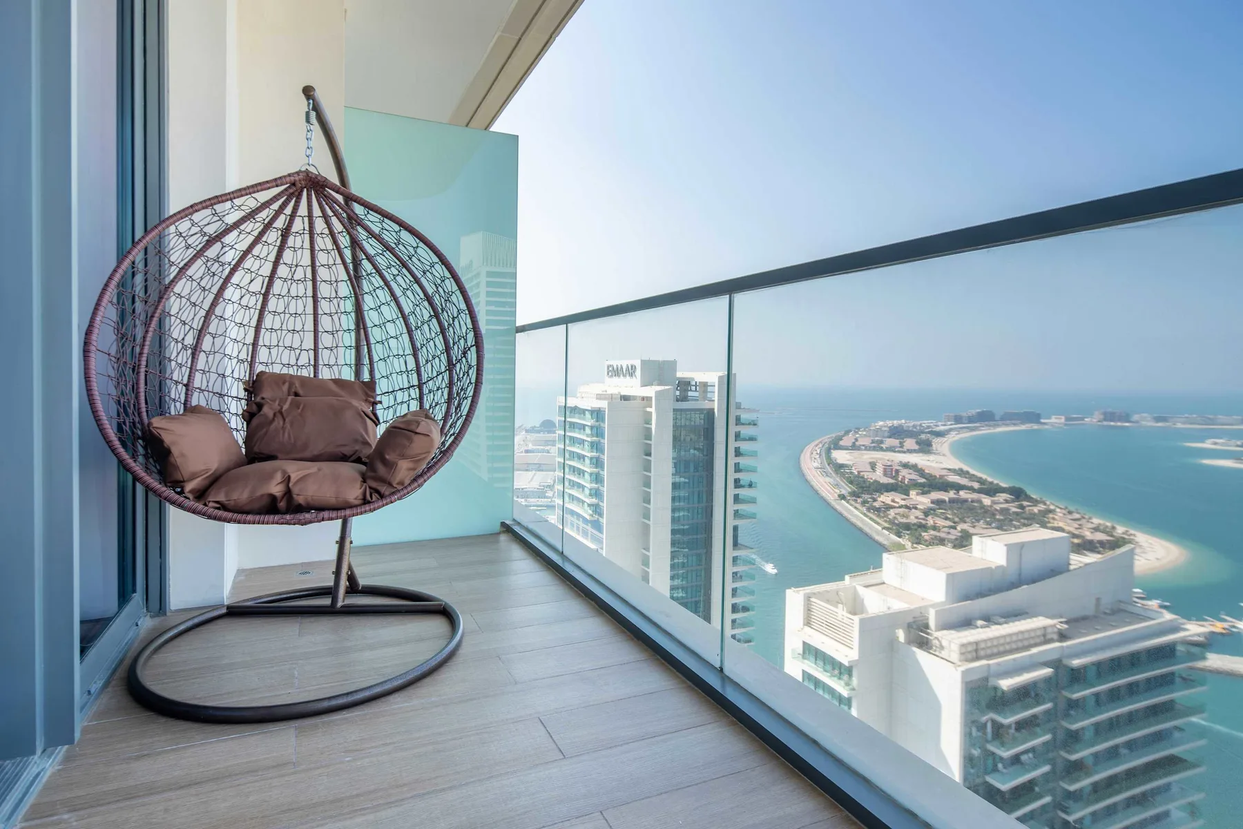 Un balcón con una silla colgante ofrece vistas al mar y a edificios cercanos.
