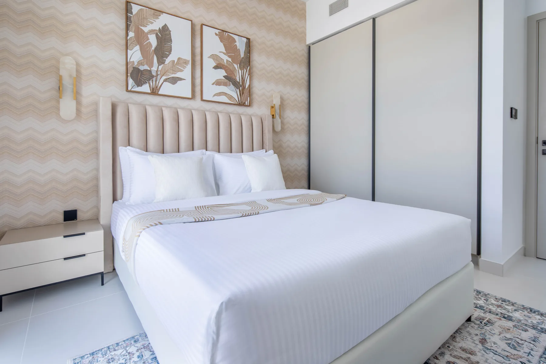 Un dormitorio con una cama bien tendida y láminas botánicas sobre el cabecero.