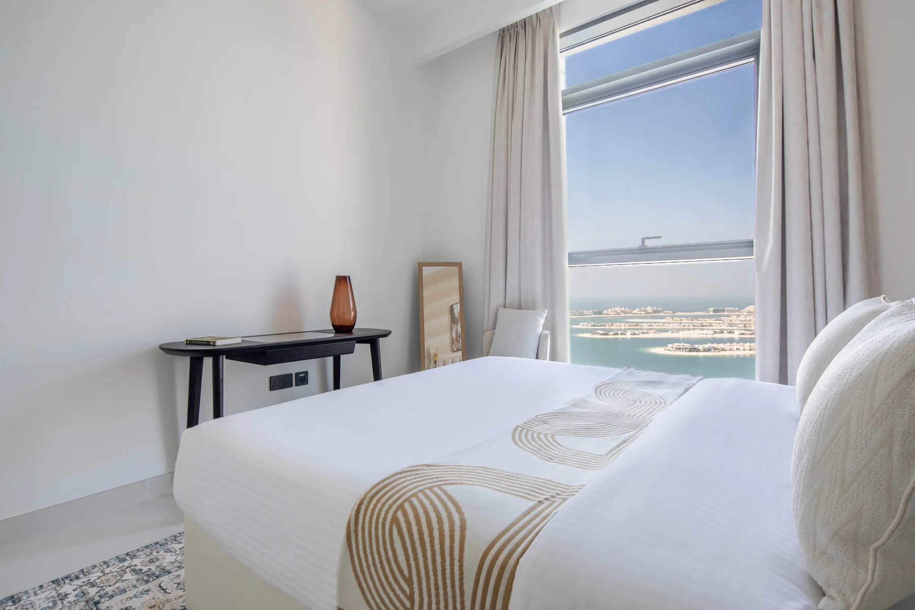 Un dormitorio luminoso con una cama bien tendida junto a una gran ventana.