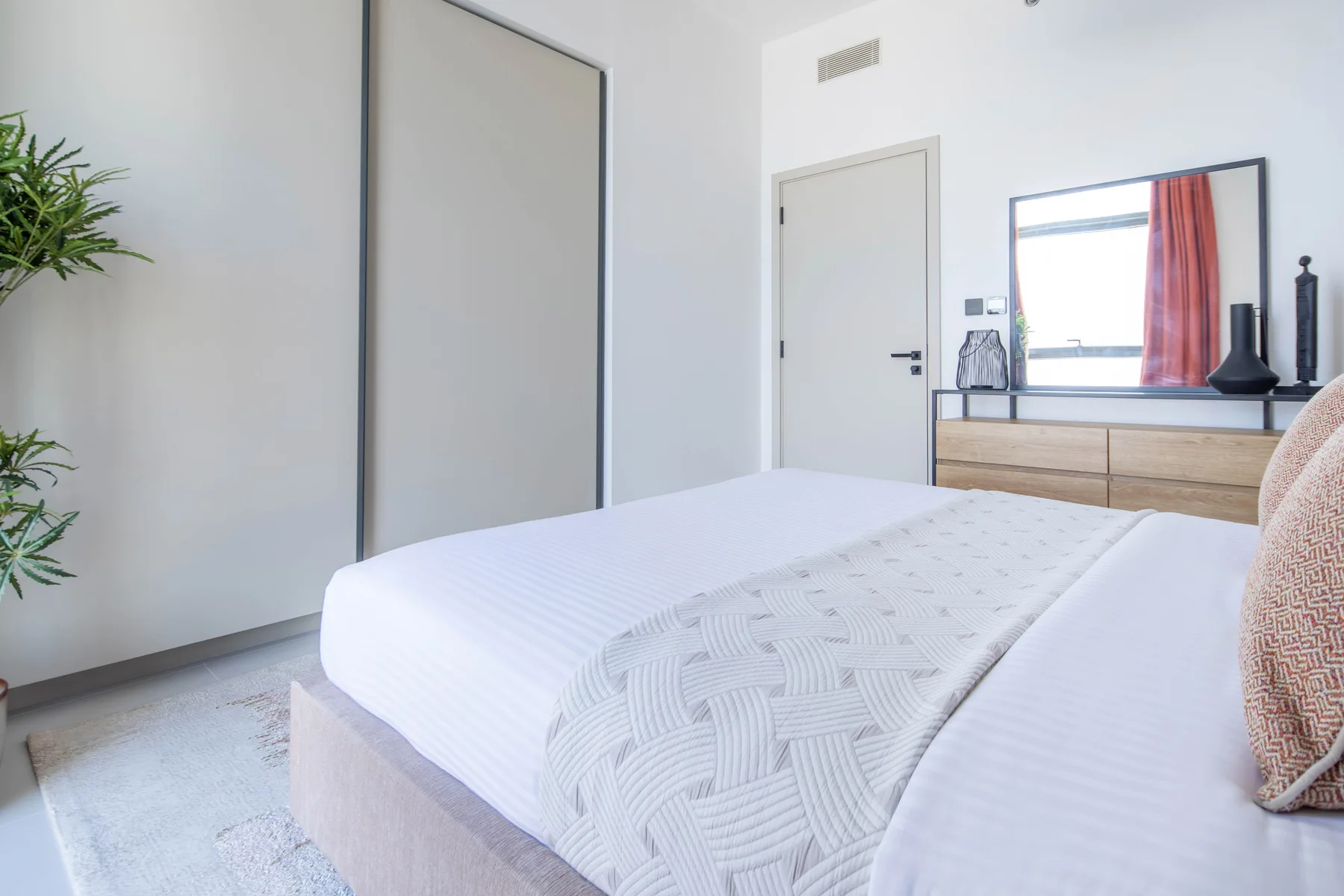 Un dormitorio luminoso con una cama bien hecha y una cómoda bajo la ventana.