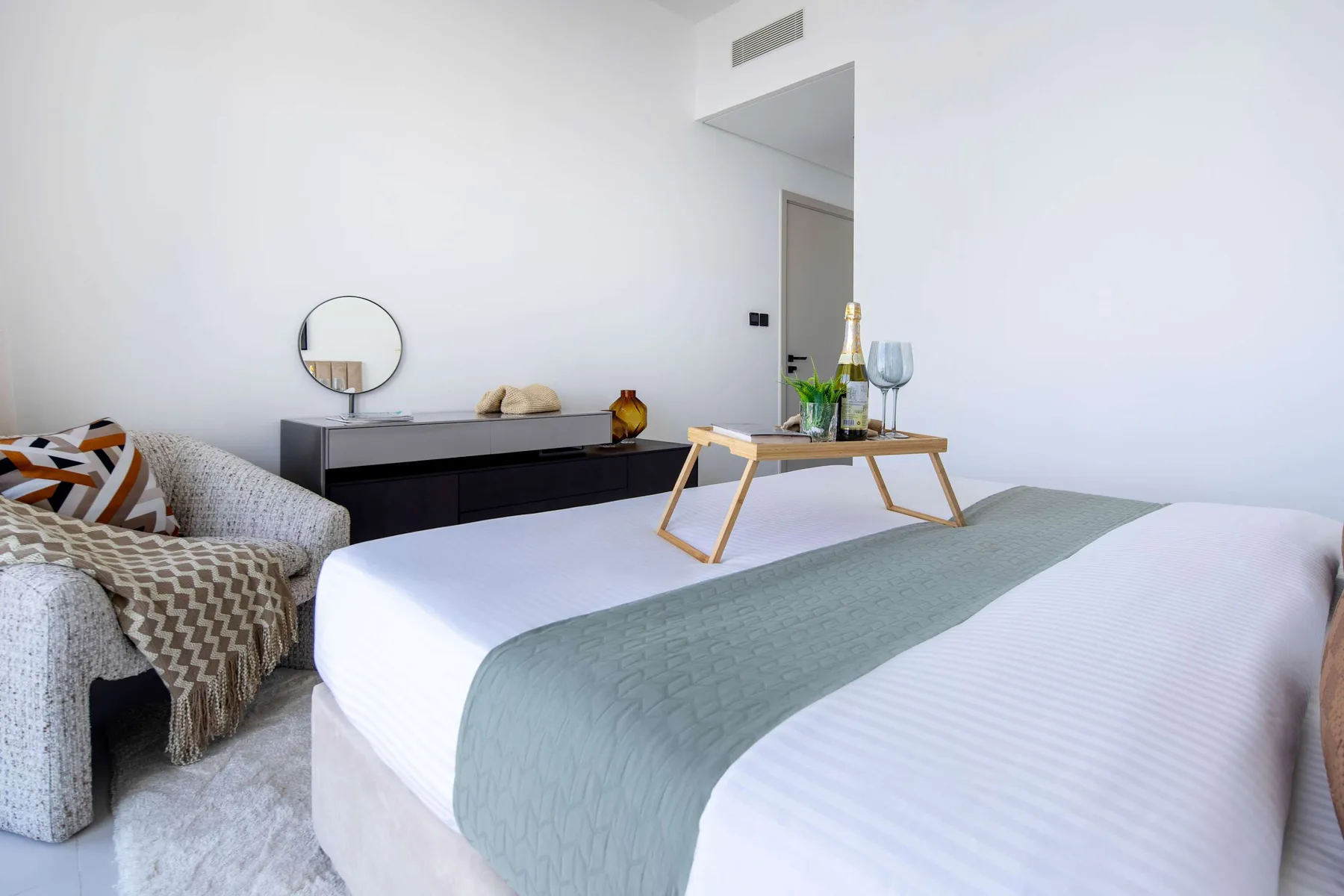 Un dormitorio luminoso con una cama tendida y una mesa pequeña junto al asiento.