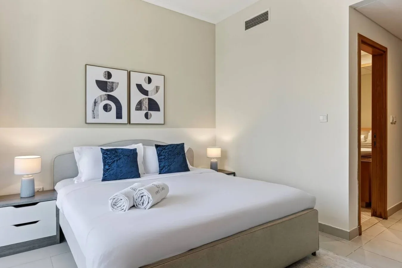 Un dormitorio con una cama bien arreglada, cojines azules y cuadros en la pared.