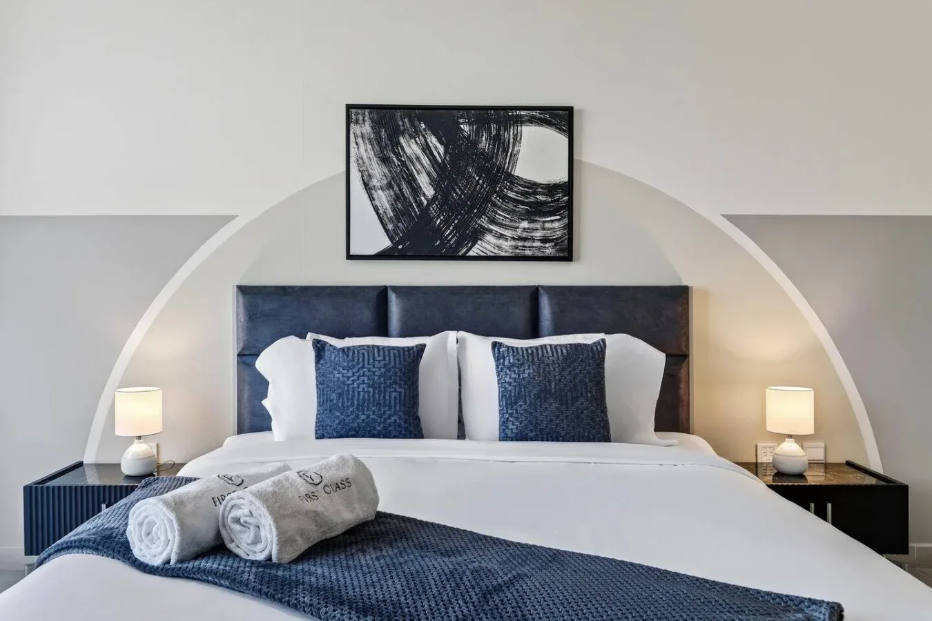 Un dormitorio con una cama bien hecha, ropa de cama azul y un cuadro sobre el cabecero.