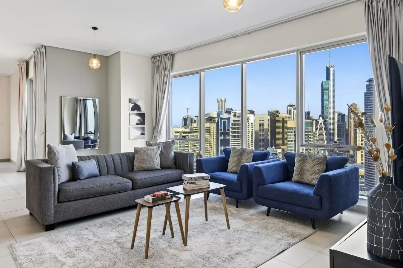 Una sala luminosa tiene asientos grises y azules junto a grandes ventanas con vista a la ciudad.