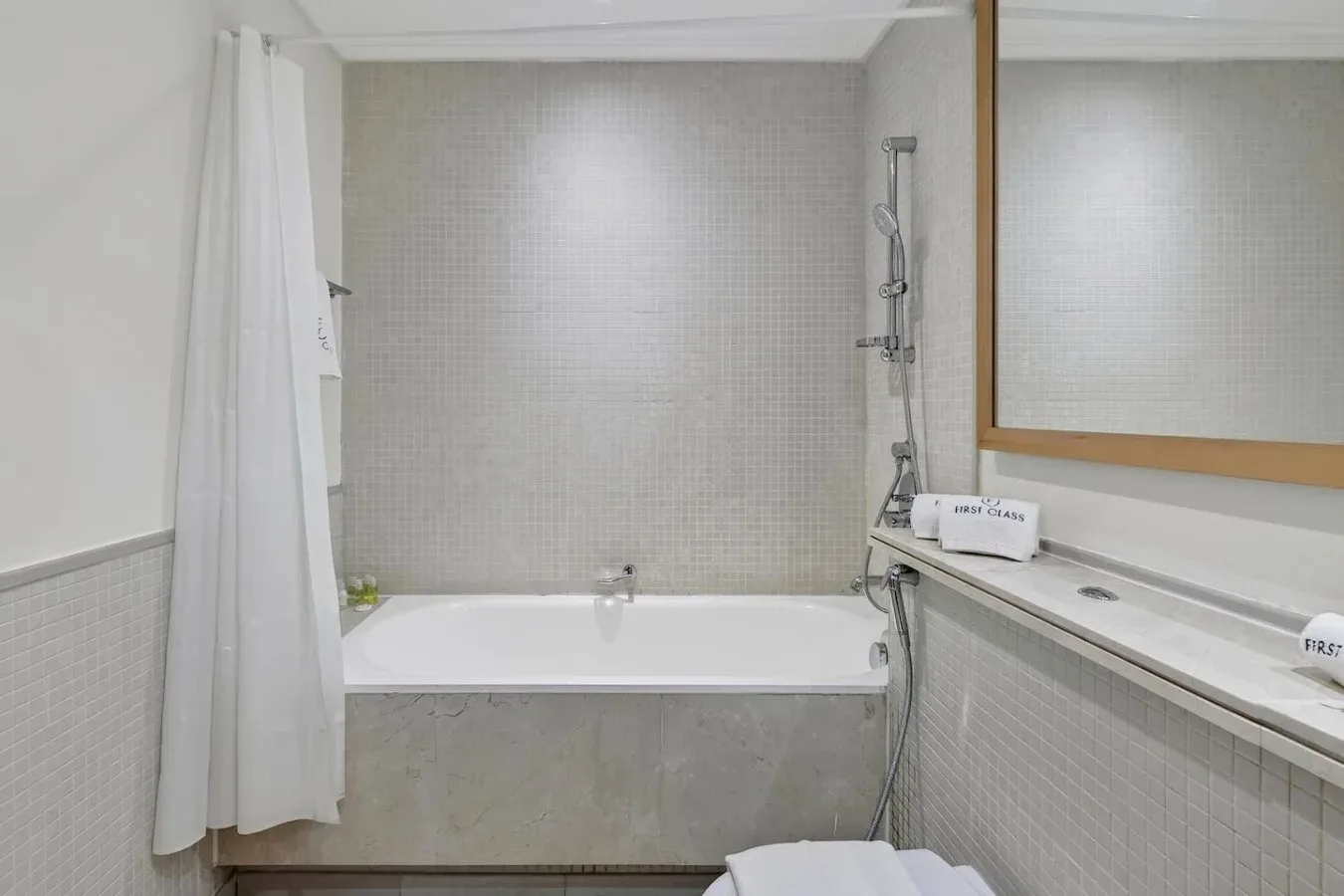 Un baño alicatado con bañera, ducha y un amplio espejo de pared.