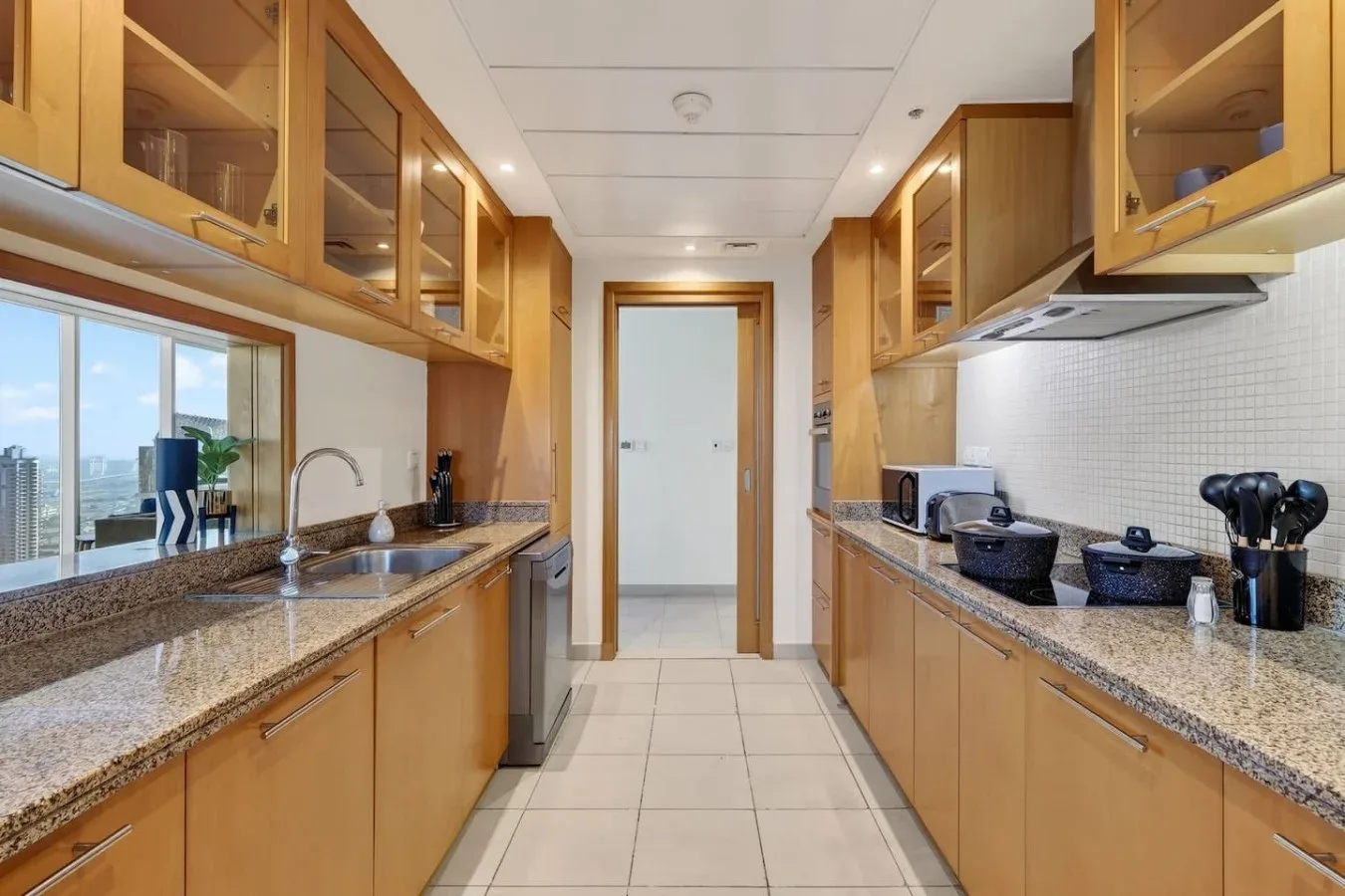 Una cocina alargada con gabinetes de madera, encimeras de piedra y una ventana.