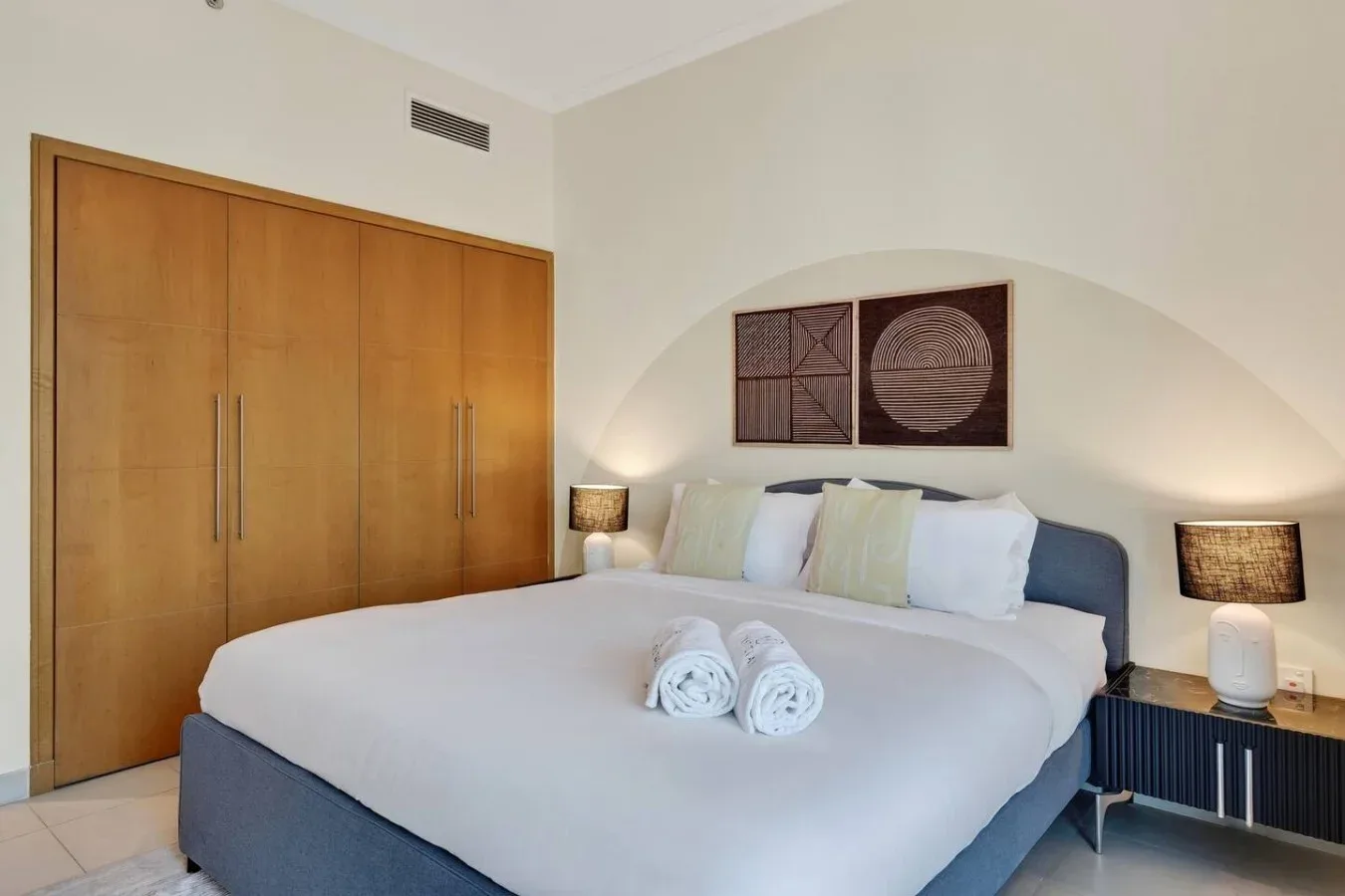 Un dormitorio con una cama bien tendida, lámparas de noche y puertas de armario de madera.