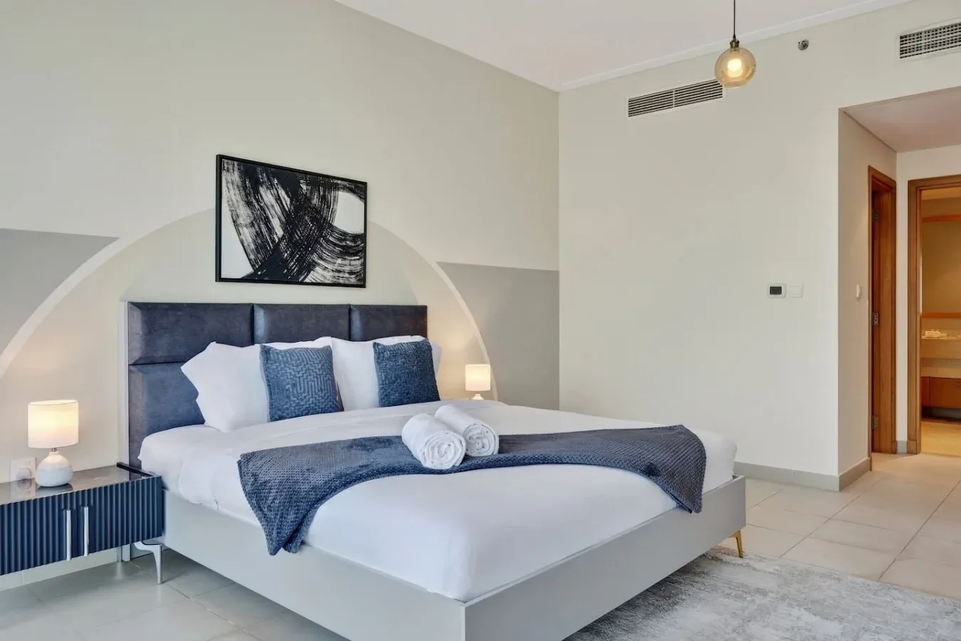 Un dormitorio con una cama tendida, ropa de cama azul y arte abstracto en la pared.