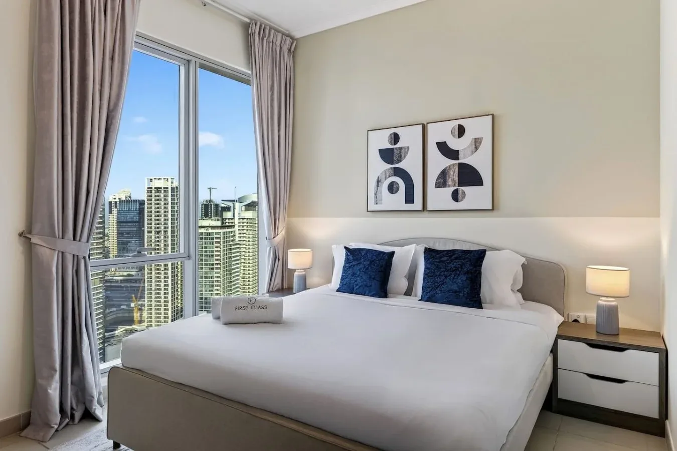 Un dormitorio con una cama grande, mesitas de noche y ventanales con vistas a edificios de la ciudad.
