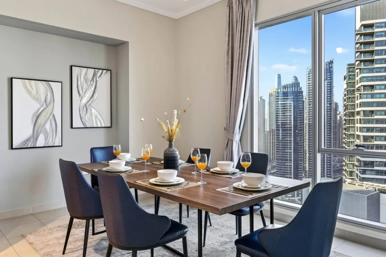 Comedor con una mesa puesta junto a grandes ventanales con vistas a edificios de la ciudad.
