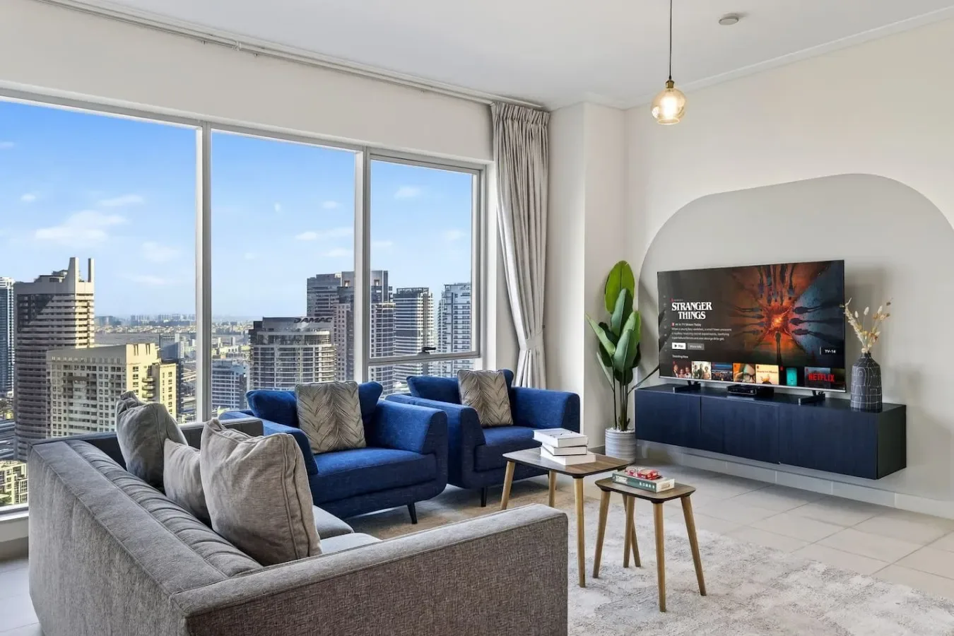 Una sala luminosa con asientos, un televisor y grandes ventanas con vistas a edificios de la ciudad.