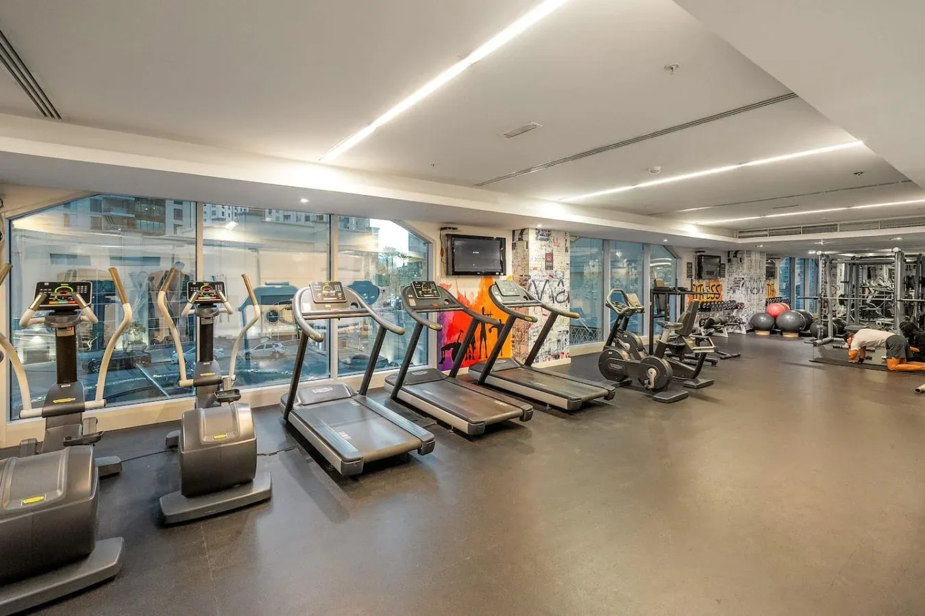 Un gimnasio con máquinas de ejercicio y grandes ventanales.