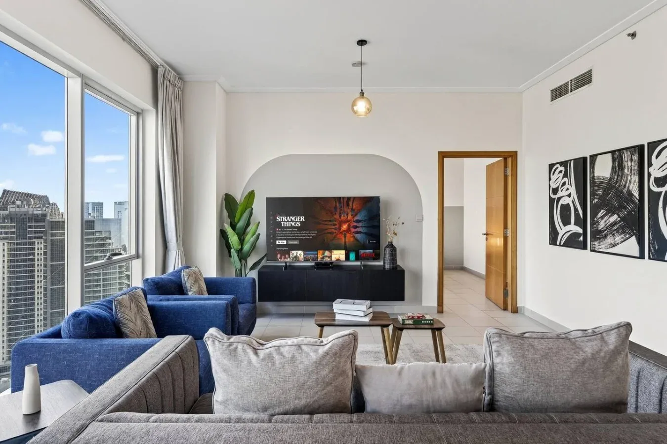 Una sala luminosa con asientos azules, un televisor y grandes ventanas.
