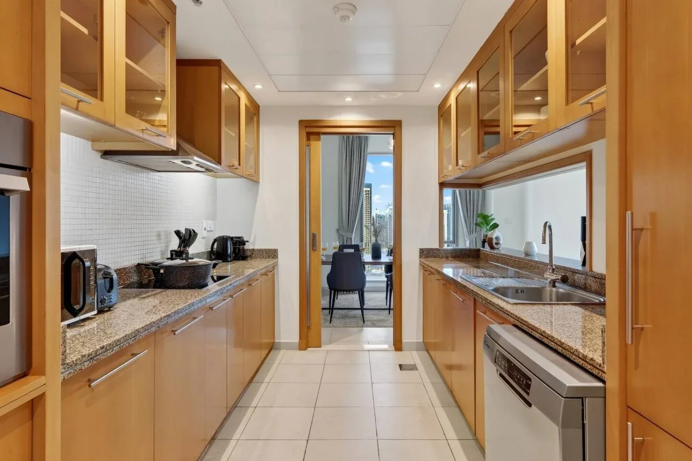 Una cocina alargada con gabinetes de madera y piso de baldosas.