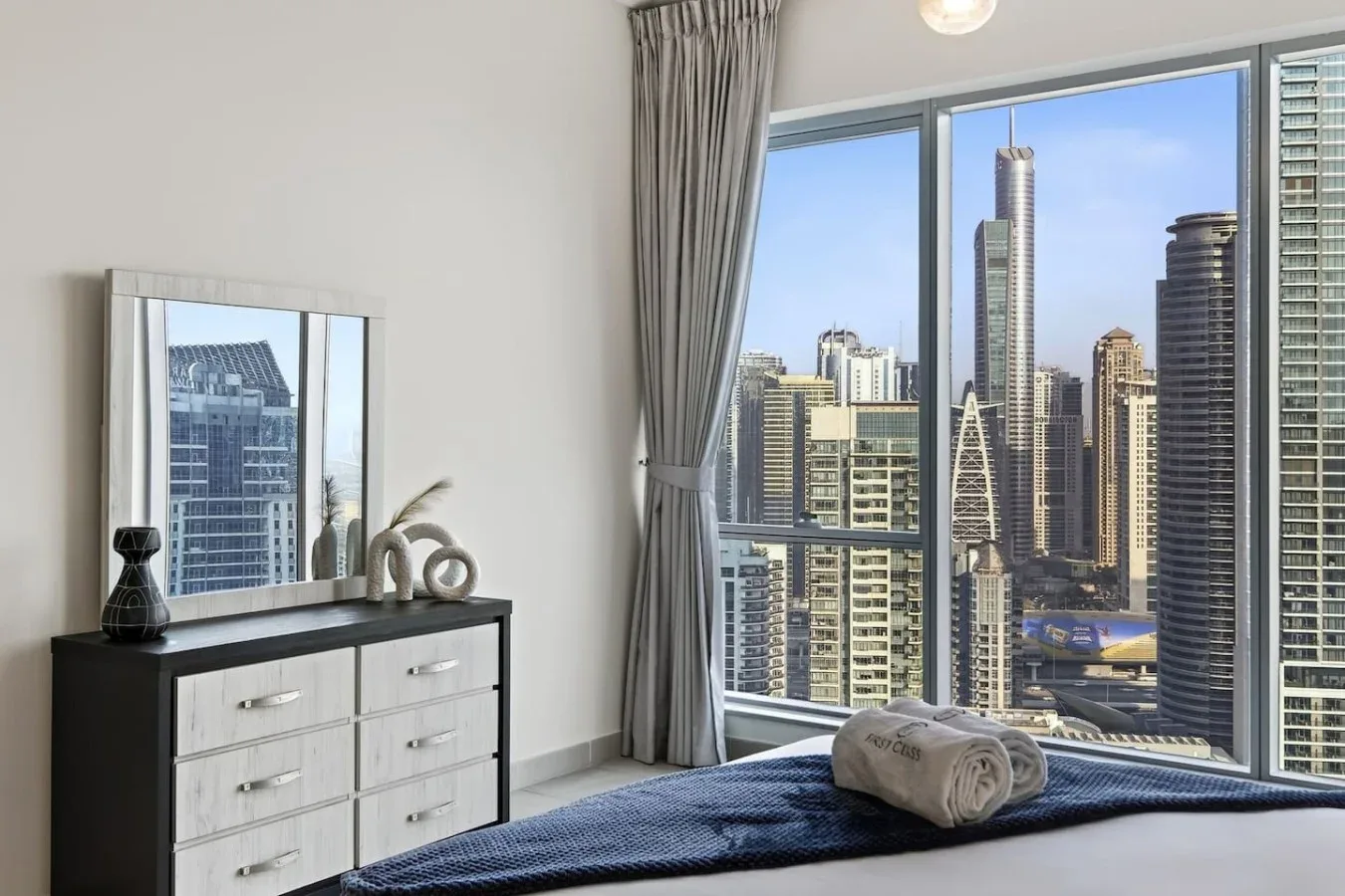 Un dormitorio con una cama junto a grandes ventanas con vistas al horizonte de la ciudad.