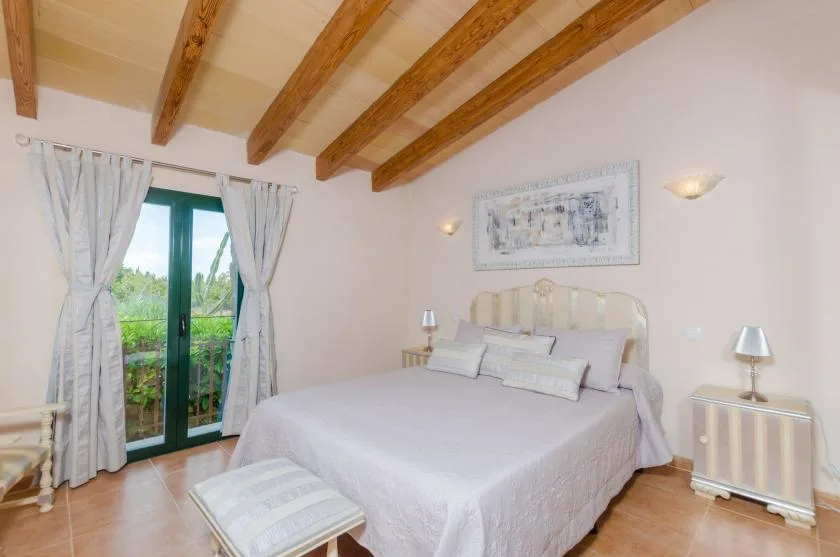 A bedroom with a bed beneath exposed wooden ceiling beams.