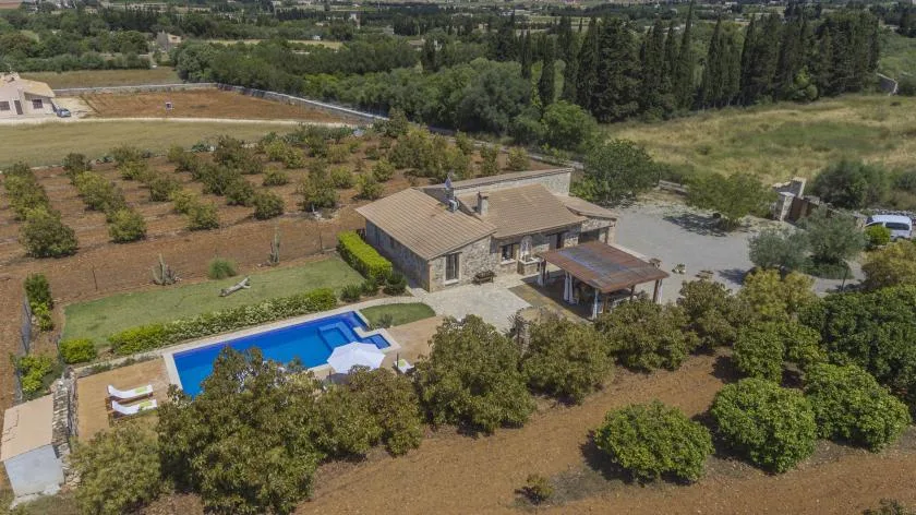 An aerial view shows a house, a blue pool, and surrounding orchards.