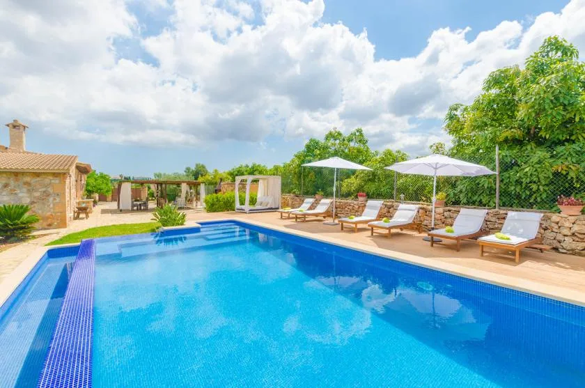 An outdoor swimming pool is surrounded by loungers and patio umbrellas.