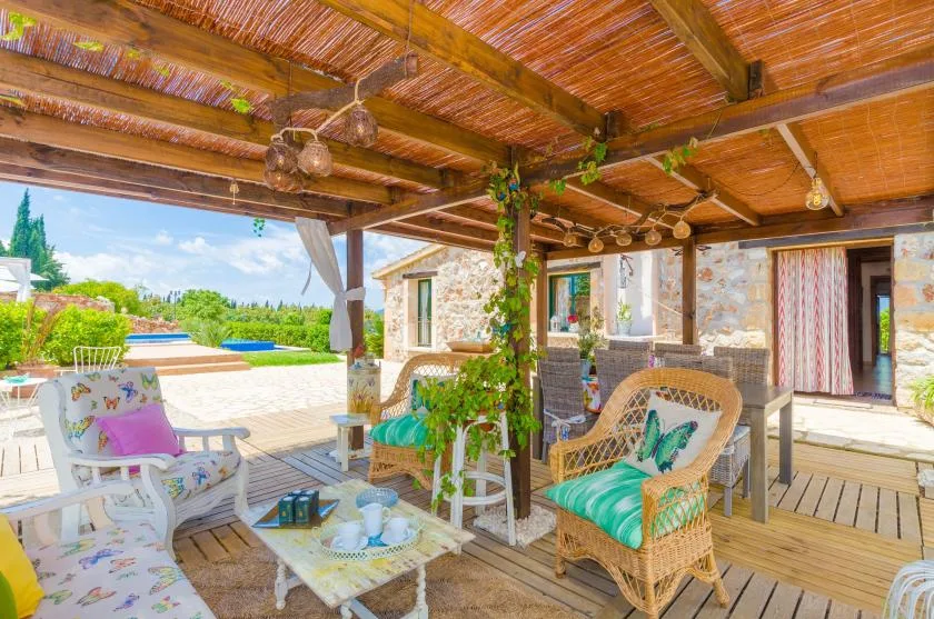 A covered patio has wicker seating and a view of the pool and garden.