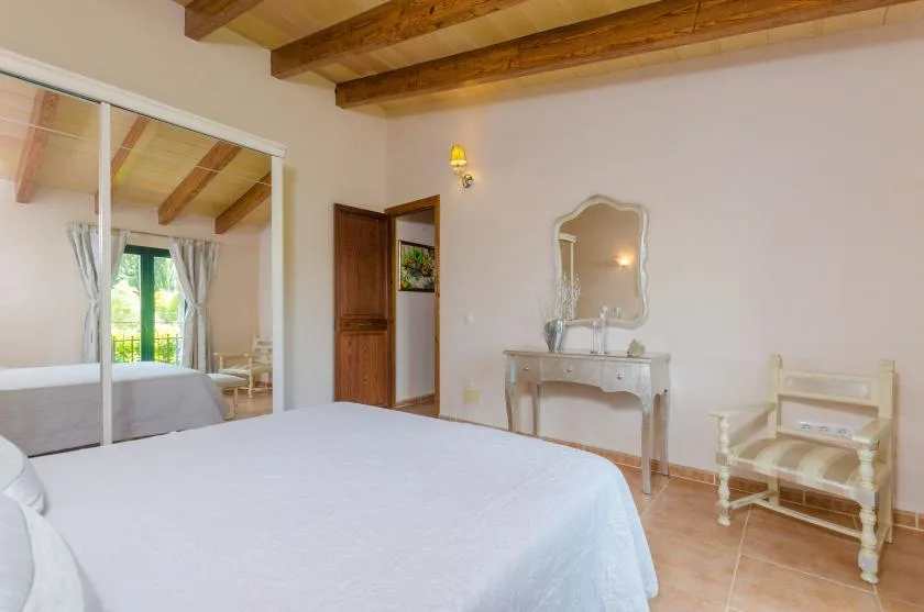 A bedroom with a large bed, mirrored wardrobe doors, and a small dressing table.