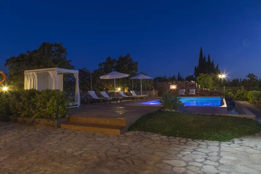 An outdoor pool area at dusk, with loungers and umbrellas on the surrounding deck.