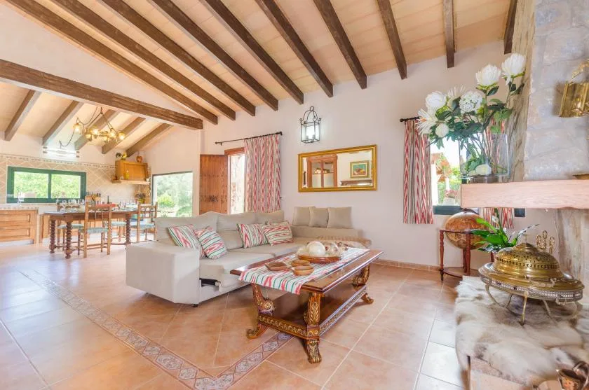 A living room opens onto a dining area, with exposed ceiling beams and a tiled floor.