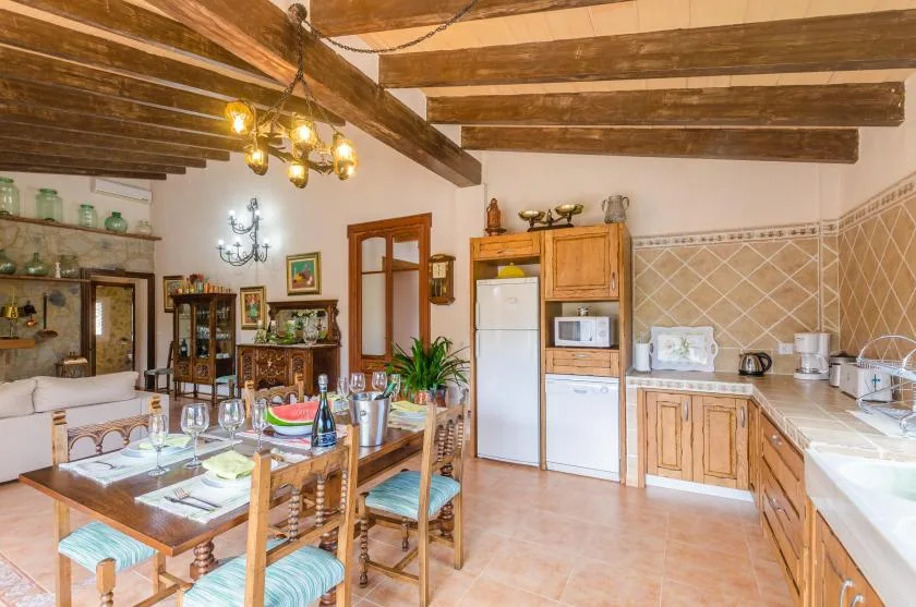 A rustic kitchen and dining area with wooden cabinetry, a table, and exposed ceiling beams.