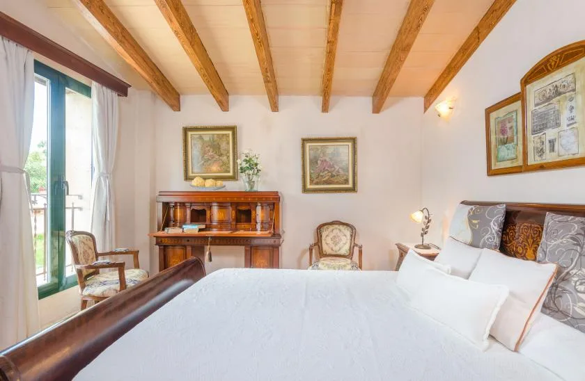 A bedroom with a bed, wooden ceiling beams, and a writing desk.