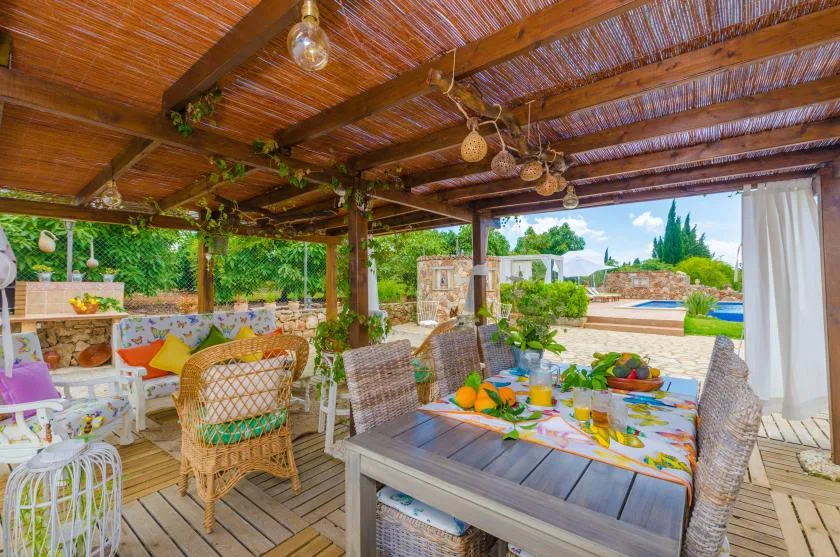 A covered outdoor dining area with wicker seating and a table overlooking a garden.