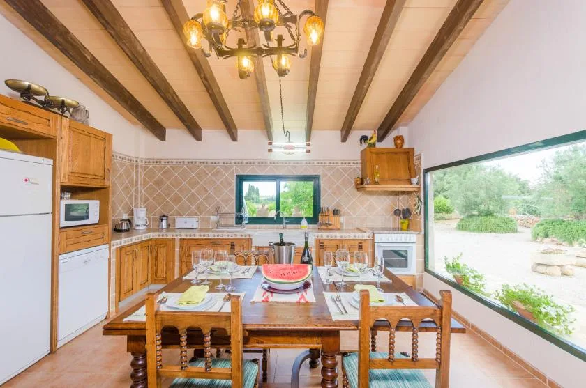 A dining area with a wooden table and kitchen cabinets beneath exposed ceiling beams.