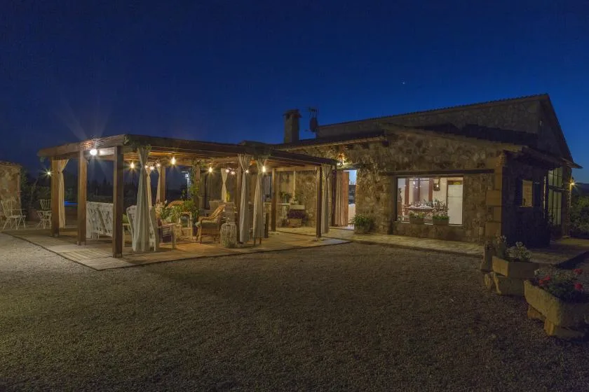 A stone building and covered outdoor seating area glow with lights at night.