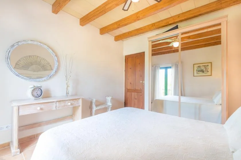A bright bedroom with a bed, exposed wooden ceiling beams, and an open doorway.