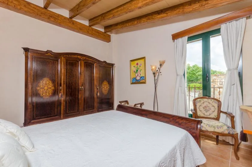 A bedroom with a large bed, dark wooden wardrobe, and glass doors opening to a balcony.