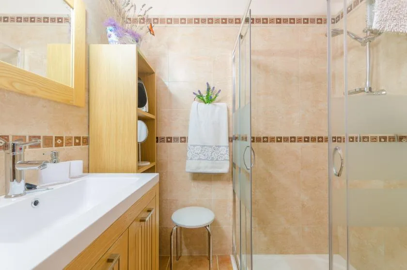 A tiled bathroom with a sink, glass shower, and towel hanging on the wall.
