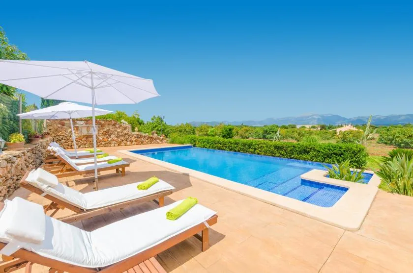 An outdoor swimming pool sits beside sun loungers and umbrellas, with green fields beyond.